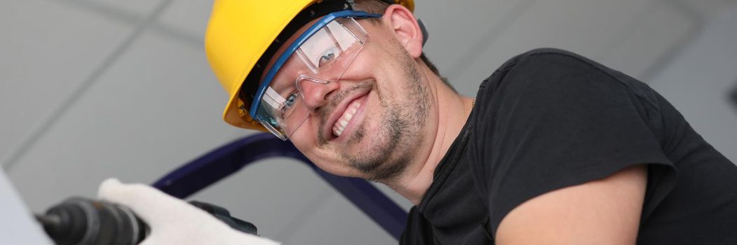 Smiling builder in helmet drilling wall in house