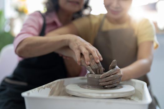 Pottery workshop. Senior teaches young asian woman pottery. Clay modeling