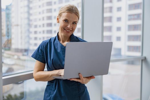 Female healthcare worker using laptop while working at doctor's office and looking camera