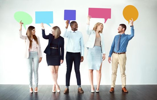 Sorry what did you say. Shot of a group of work colleagues standing next to each other while holding speech bubbles against a white background.