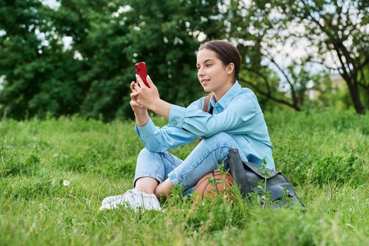 Teenage female student sitting on the grass using smartphone.