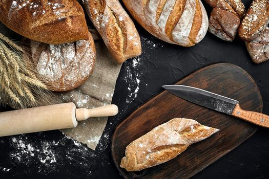 Fresh bread, wooden board and cutting knife on black table