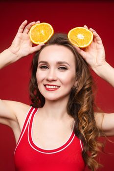 Beautiful woman in a red swimsuit with bright makeup and red lips with orange slices, summer, brightness, joy