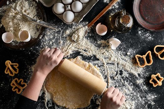 Female hands rolling dough with a rolling pin on a black table. Top view