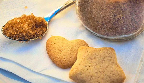 Brown sugar in a teaspoon for tea or coffee with heart and star shaped biscuits on a table in a cafe