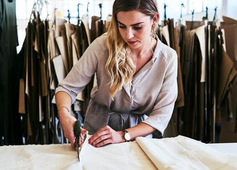 Cropped shot of a young fashion designer cutting fabric in her workshop.