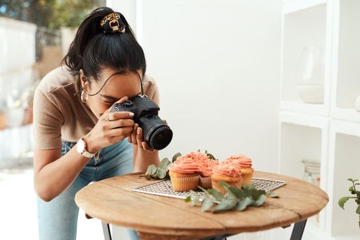 Getting close enough to capture the details. Cropped shot of an attractive young businesswoman using her camera to photograph cupcakes for her blog.