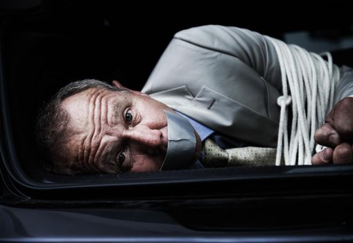Help me.... Portrait of a frightened businessman lying bound and gagged in the trunk of a car.