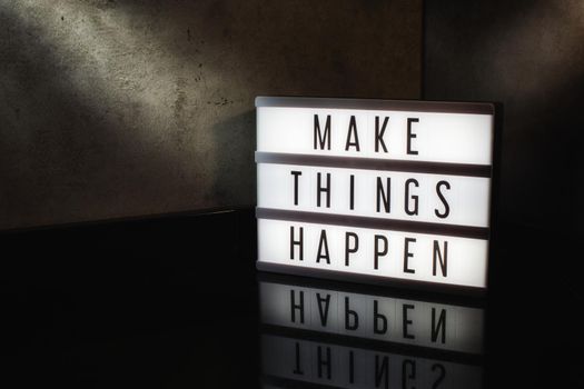 Make things happen motivational message on a light box in a cinematic moody background