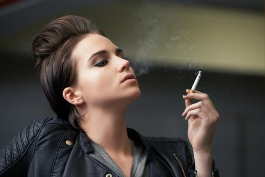Attitude and attractive. Shot of a rebellious looking young woman smoking a cigarette in a car garage.