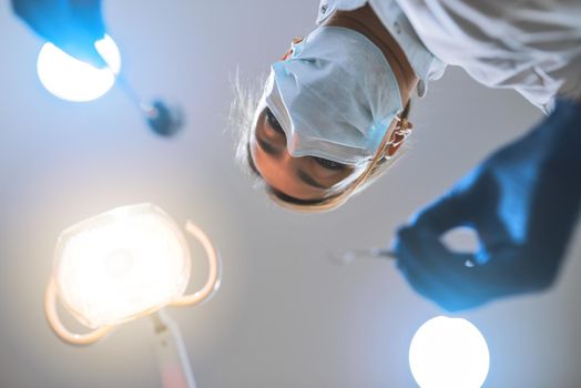 Just remain calm and Ill do the rest. Low angle shot of a focused young female dentist wearing a surgical mask while attempting to work on a patients teeth.