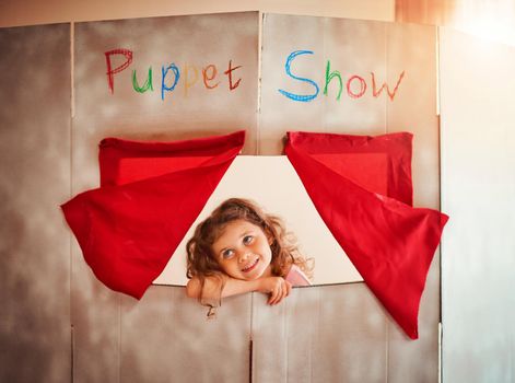 Fostering a childs imagination through play. Shot of an adorable little girl standing in the window of a puppet show theatre at home.