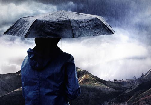 A storm is brewing. Shot of a woman covered with an umbrella watching a thunderstorm over a mountain.