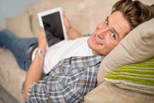 Creature comforts.... Shot of a handsome young man using his digital tablet while relaxing on the sofa.