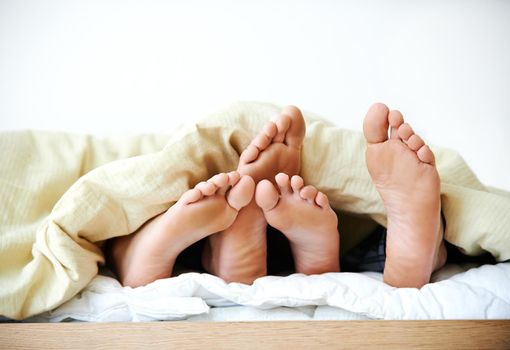Were going to need a bigger bed. Cropped shot of a couples feet poking out from under the bedsheets.