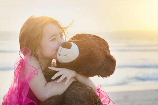 The innocence of childhood. Portrait of a cute little girl playing with her teddy bear on the beach.