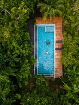 couple men and woman in swimming pool in the jungle of Krabi Thailand, aerial view with drone above swimming pool in jungle of Thailand