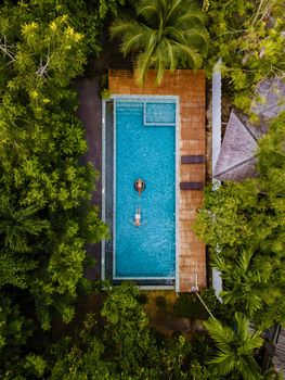 couple men and woman in swimming pool in the jungle of Krabi Thailand, aerial view with drone above swimming pool in jungle of Thailand