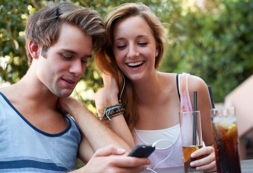 Socialising in the twenty first century. Cute teen couple sharing an MP3 player and listening to music while enjoying their beverages.