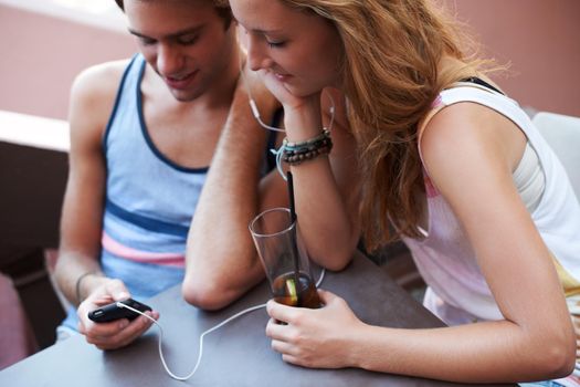 Get closer to your crush through the wonders of technology. Happy teen couple sharing an MP3 player and listening to music while enjoying their beverages.