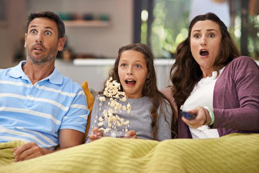 They love scary movies. Shot of a family sitting on their living room sofa watching a movie and eating popcorn.