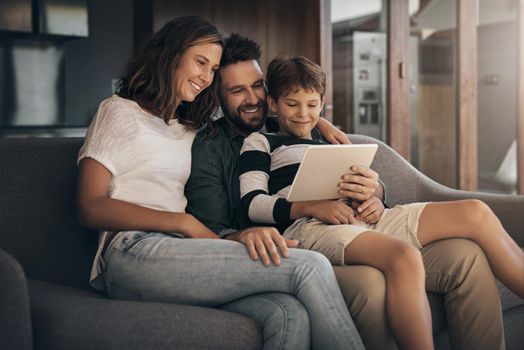 Share the love, share the fun. Shot of an adorable little boy using a digital tablet with his mother and father on the sofa at home.