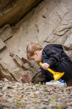 A boy-child on the background of a rocky mountain looks at something with curiosity and is surprised. Nature, rocks, mountains.