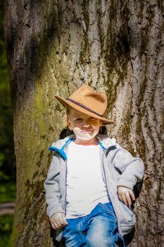 Cute boy posing in a cowboy hat in the woods by a tree. The sun's rays envelop the space. Interaction history for the book. Space for copying
