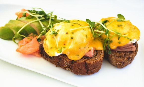 Eggs Benedict on brown bread toast with smoked salmon and sliced avocado