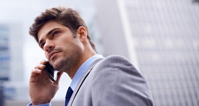 A smart phone for a savvy businessman. A low angle shot of a handsome young businessman using his cellphone in the city.