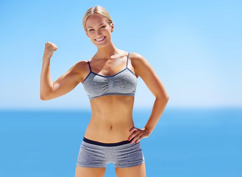 Looking good. Portrait of an attractive young woman in exercise clothing flexing her bicep outside.