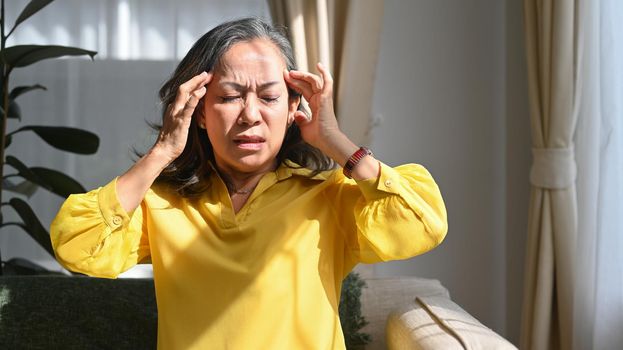 Upset mature woman touching her head suffering from head ache, migraine or dizziness. Age, medicine, health care and people concept