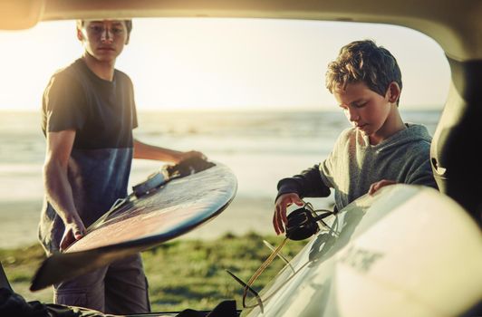 We surf, therefore we are. Shot of two young brothers unloading their surfboards from the back of a car by the beach.