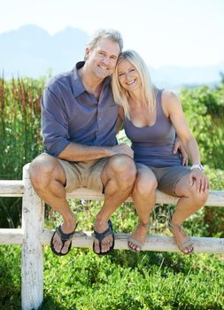 Loving the outdoors. A happy mature couple sitting on a fence outdoors.