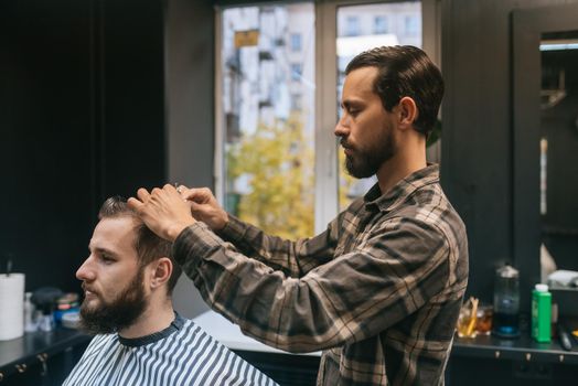 Cheerful young bearded man getting haircut by hairdresser at barbershop