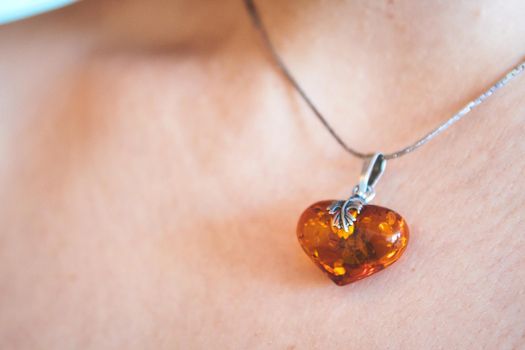 A heart shaped amber pendant worn around the neck of a young woman