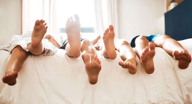 Putting their feet up after a day of fun. Closeup shot of children lying barefoot on a bed at home.