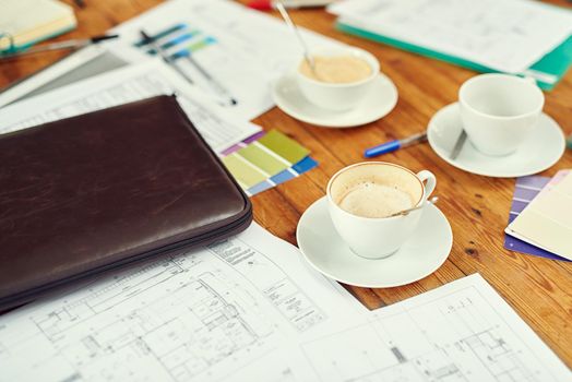 An architects natural habitat. Shot of cups of coffee, blueprints and color swatches on a desk.
