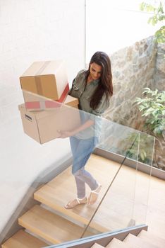 Honey, the movers are here. A young woman carrying cardboard boxes in her home.