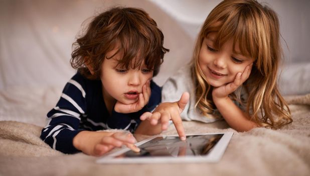 Boardgames gone digital. Shot of two adorable siblings using a digital tablet while lying on a bed.