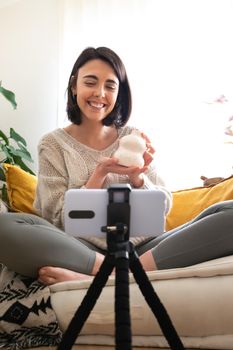 Young caucasian woman DIY influencer showing handmade artisan ceramic vase at camera recording online video. Vertical.