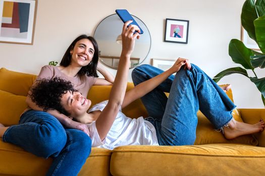 Young lesbian couple taking selfie at home living room using mobile phone.