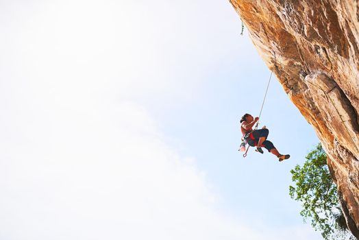 Life is better lived on the edge. Shot of a young rock climber scaling a cliff face.