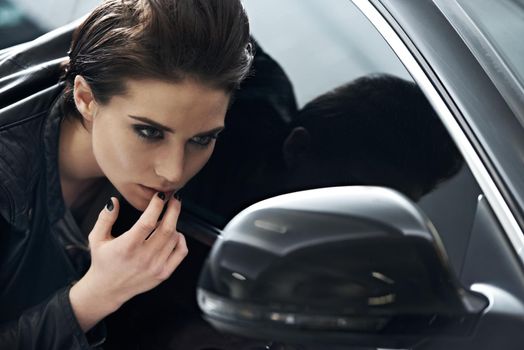 Attitude meets style. Shot of an attractive young woman looking at her reflection in the side mirror of a car.