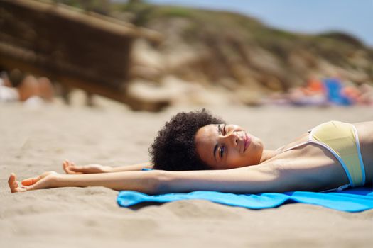 Content young African American woman lying on sandy beach and winking at camera