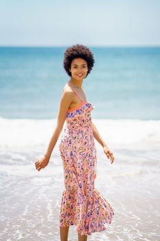 Stylish black woman standing on sandy beach