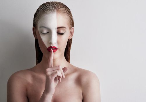 Beauty is art. Shot of a beautiful woman wearing face paint and red lipstick against a plain background.