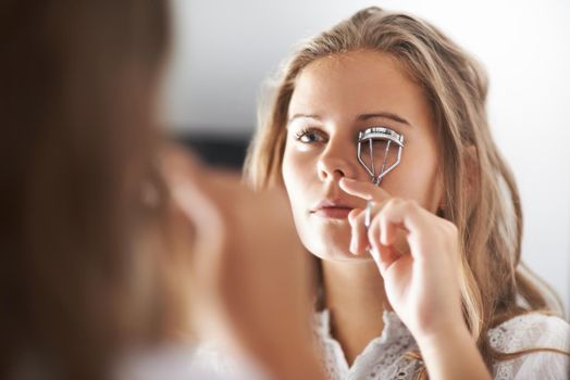 Enhancing her natural beauty. A teenage girl curling her eyelashes in the mirror.