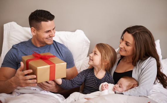 Happy birthday daddy. Shot of a happy family giving their father a gift in bed.