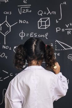 child scientist in lab coat writing on blackboard
